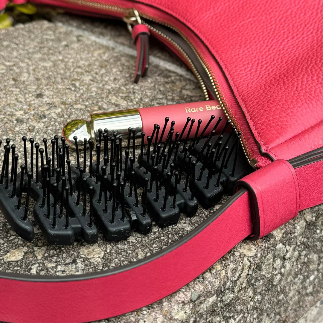 Black flex-frame detangling brush and lipstick tucked in a pink handbag